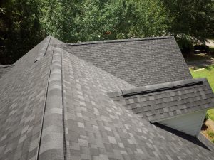 Image from atop a residential roof with granite black aphalt shingles. Green grass and trees in background.