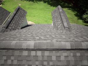Image from top of a residential roof with granite black aphalt shingles. Green grass yard in background.